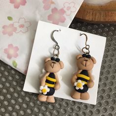 a pair of earrings with a teddy bear wearing a bee costume and holding a flower