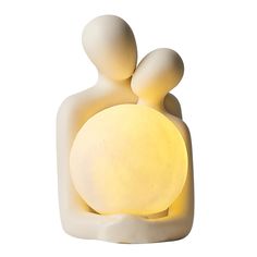 a small white sculpture with a yellow light on it's face and two people holding each other