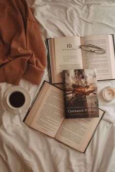 an open book sitting on top of a bed next to a cup of coffee and two books