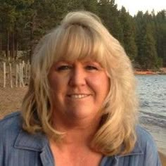 a woman standing on the beach with trees in the back ground and water behind her