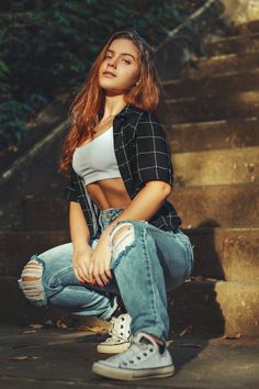 a young woman sitting on the steps with her hands in her pockets and looking up