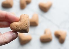 a hand holding a heart shaped cookie in front of small hearts on a white surface