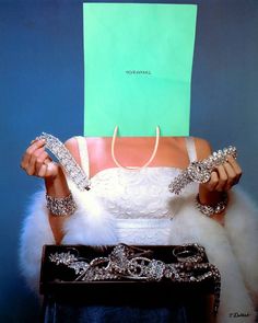 a woman holding up a green paper bag over her head with jewelry on the table in front of her