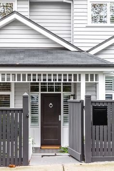 a white house with a brown door and black fence on the front porch is seen in this image