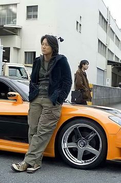 a man standing next to an orange sports car