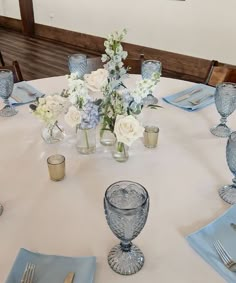 a white table with blue napkins, silverware and flowers in vases on it