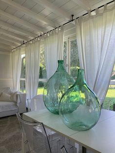 two green vases sitting on top of a white table in front of a window