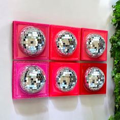 four red boxes with mirrored disco balls in them on a white wall next to a green plant