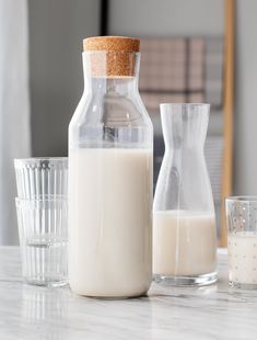 a bottle of milk next to two glasses on a table with a corked top