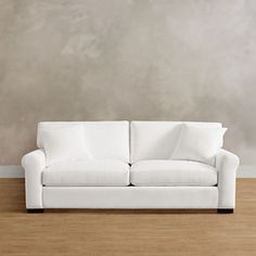 a white couch sitting on top of a hard wood floor next to a gray wall