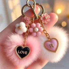 a hand holding a pink and black heart shaped keychain with pom - poms