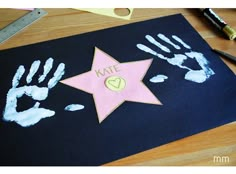 handprints on a black paper with pink star and green heart next to scissors