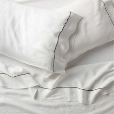 an unmade bed with white sheets and black piping on the pillowcases