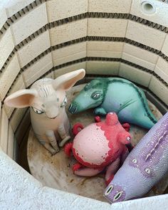 three stuffed animals sitting in a small round container with tile walls and flooring around them