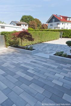 an outdoor patio area with stone pavers and trees in the back ground, surrounded by hedges