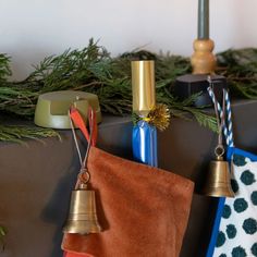 christmas stockings and bells hanging from hooks on a mantle with evergreen branches in the background