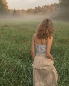 a woman standing in the middle of a foggy field with her back to the camera