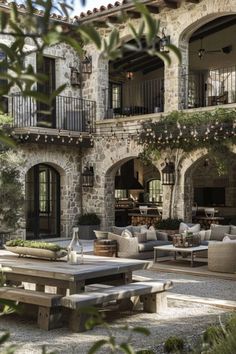 an outdoor seating area with tables and benches in front of a stone building that has several balconies on it