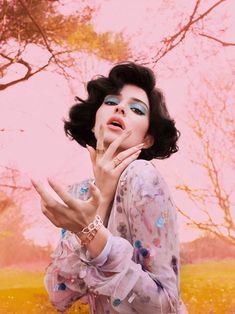 a woman with black hair and blue eyes is posing for a photo in front of trees