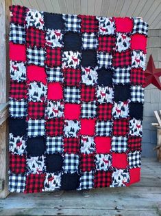 a red, black and white quilt hanging on the side of a wooden fence next to a star