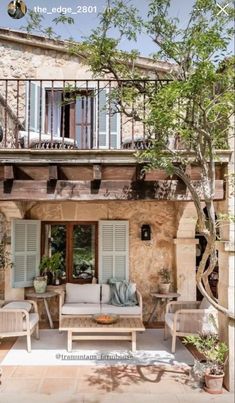 an outdoor living area with furniture and plants on the outside wall, in front of a stone building