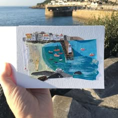 a person holding up a card with boats in the water