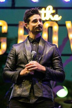 a man holding a microphone while standing in front of a neon sign