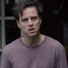 a man in a grey shirt is looking at the camera