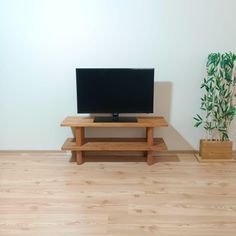 a flat screen tv sitting on top of a wooden stand next to a potted plant