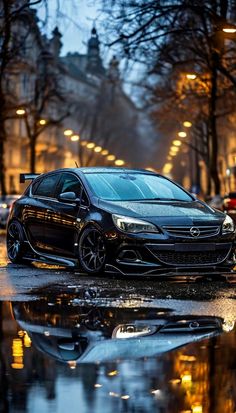 a black car parked on the side of a wet street next to some trees and buildings