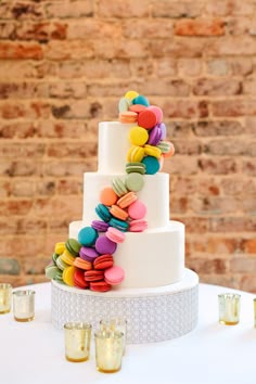 a white wedding cake with colorful buttons on the top and bottom tier is surrounded by candles