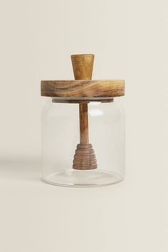 a glass jar with a wooden top and handle on the bottom that has a small piece of wood sticking out of it