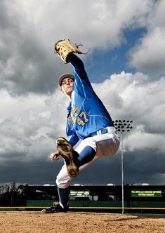 a baseball player pitching a ball on top of a dirt field with clouds in the background