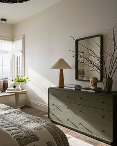 a bedroom with a dresser, mirror and lamp in it's corner next to a window