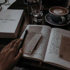 a person is writing in a book with a pen and cup of coffee on the table