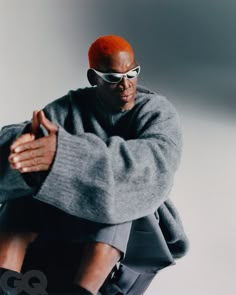 a man with red hair and sunglasses sitting on a chair in front of a white wall