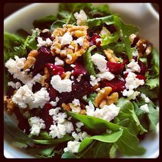 a white bowl filled with salad topped with feta cheese and cranberries