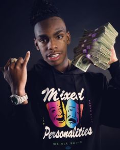 a young man holding stacks of money in front of his face and wearing a black hoodie