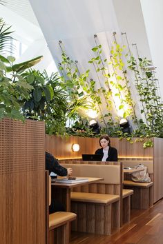 a woman sitting at a table in a restaurant with plants on the wall above her