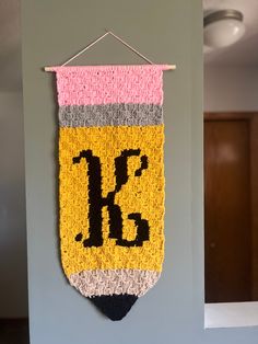 a crocheted banner hanging on a wall with the letter k in black and yellow