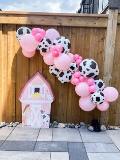 a cow themed birthday party with pink and white balloons, farm animals and a barn