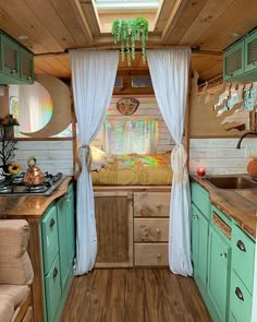 an interior view of a small camper with wood floors and green cabinets, white drapes on the windows