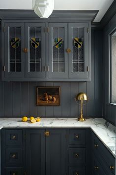 a kitchen with gray cabinets and marble counter tops, gold accents on the door knobs