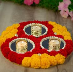 three candles are placed in the center of a decorative tray with red, yellow and white flowers