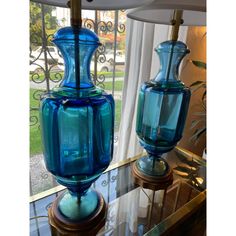 two blue vases sitting on top of a glass table next to a lamp shade