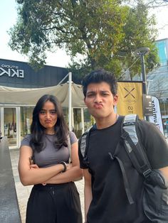 two people standing in front of a building with their arms crossed and looking at the camera