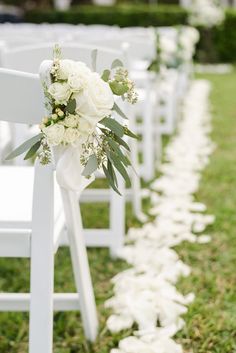 rows of white chairs with flowers and greenery lining the aisle for an outdoor ceremony