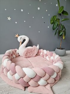 a pink and white swan shaped bed on top of a wooden floor next to a potted plant