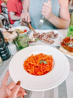 a person holding a fork over a plate of food on a table with other people