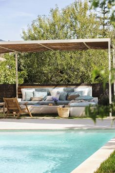 a couch sitting next to a swimming pool under a wooden pergoline covered roof